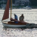 Two people are on a small sailboat near a dock, preparing or securing the sail.