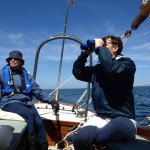 Two people on a sailboat, one using binoculars, the other steering. Related to the Shaheen Portman Energy Efficiency Legislation