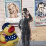 A mural featuring classic film icons and a rubber duck wearing a patriotic outfit in the foreground.